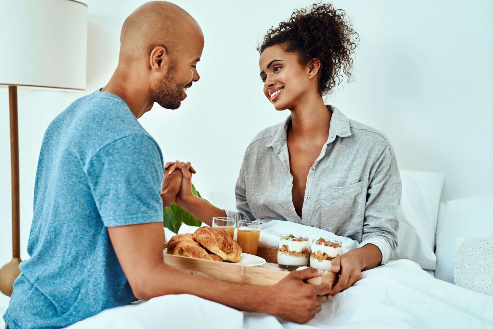 Een man en vrouw die "De liefdestaal van dienstbaarheid" tentoonstellen door een dienblad met eten in bed vast te houden.