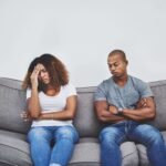 Een zwarte man en vrouw zitten op een grijze bank en tonen een emotionele band.