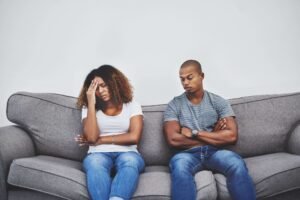 Een zwarte man en vrouw zitten op een grijze bank en tonen een emotionele band.